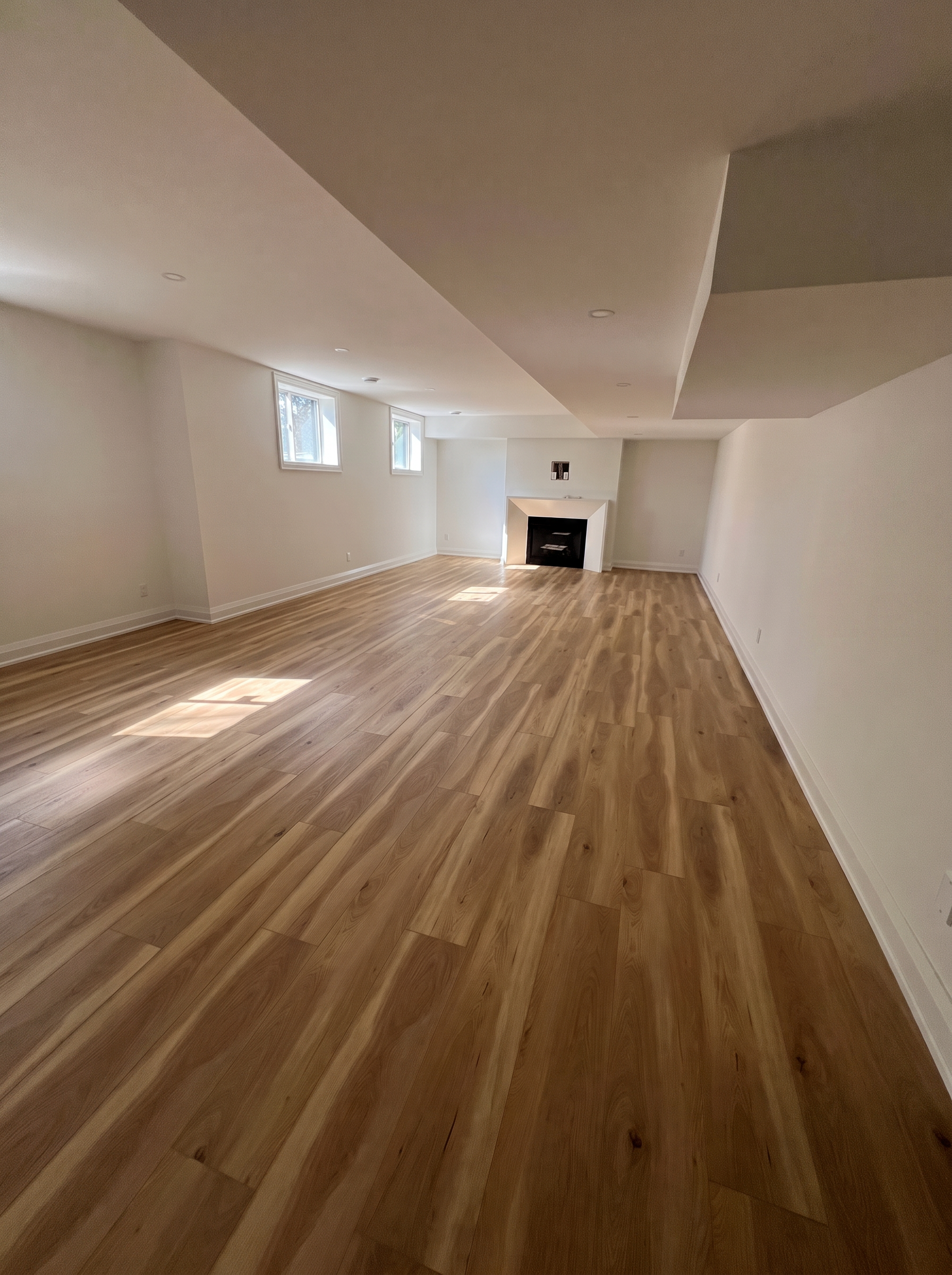 Completed basement with wood flooring, fireplace and clean white walls in Niagara
