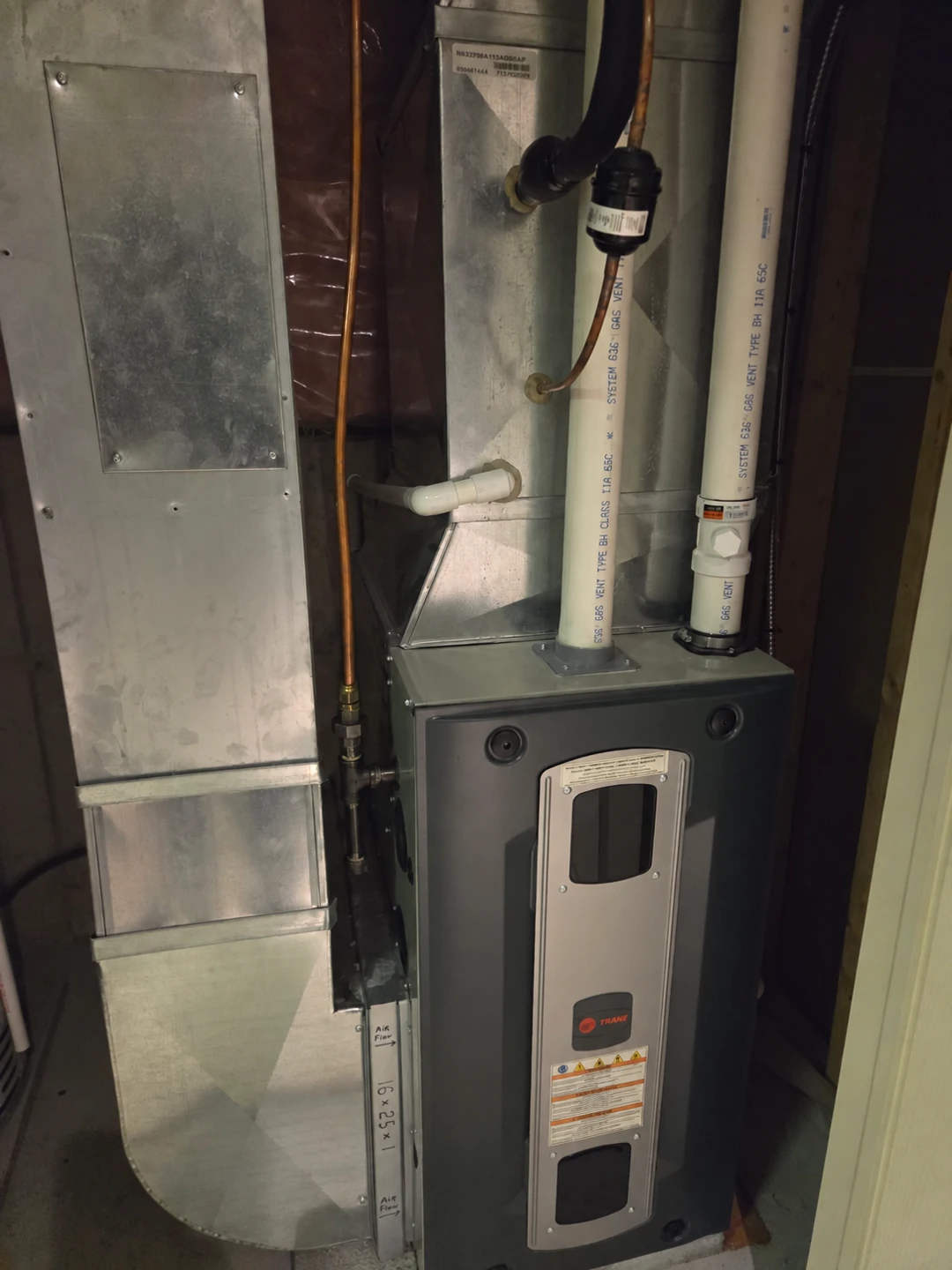Trane furnace beside sheet-metal ductwork with PVC venting and copper connections